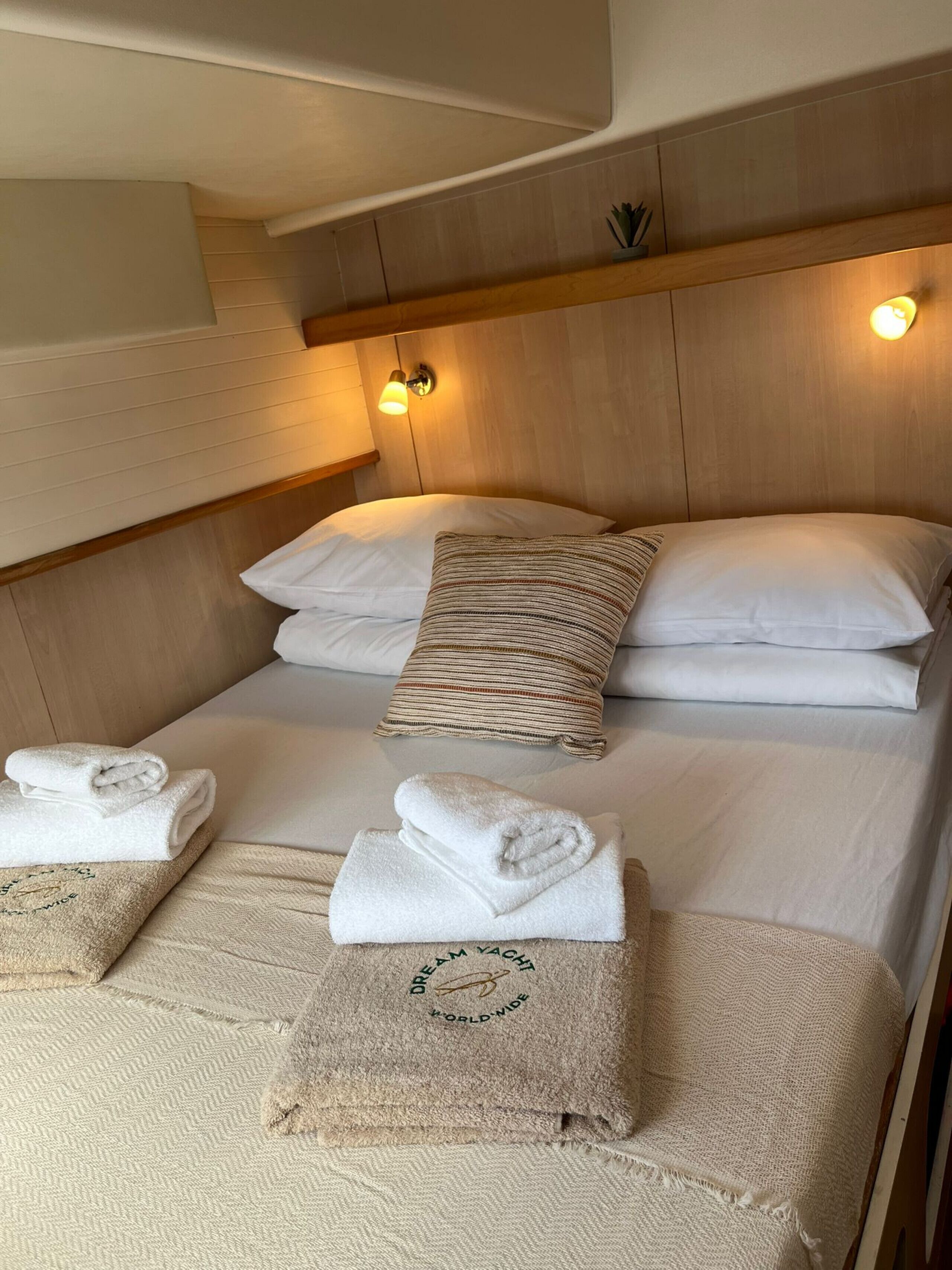 A bunk bed with two white pillows and a striped pillow, a headboard with wall-mounted lights, and neatly folded towels on the lower bunk.