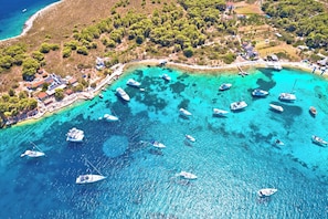 An aerial view of a coastal area with boats docked along the shore, surrounded by greenery and buildings. - Sun-Kissed Sailing Adventure in Mlini, Croatia (Srebreno)