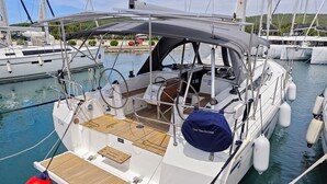Eine Segelyacht liegt in einer Marina festgemacht, mit einer überdachten Deckfläche, einer Sitzecke und einem kleinen Tisch.