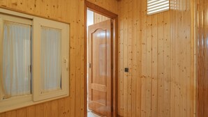 A wooden interior hallway with a checkered floor, a door with a window, and a light switch on the wall.