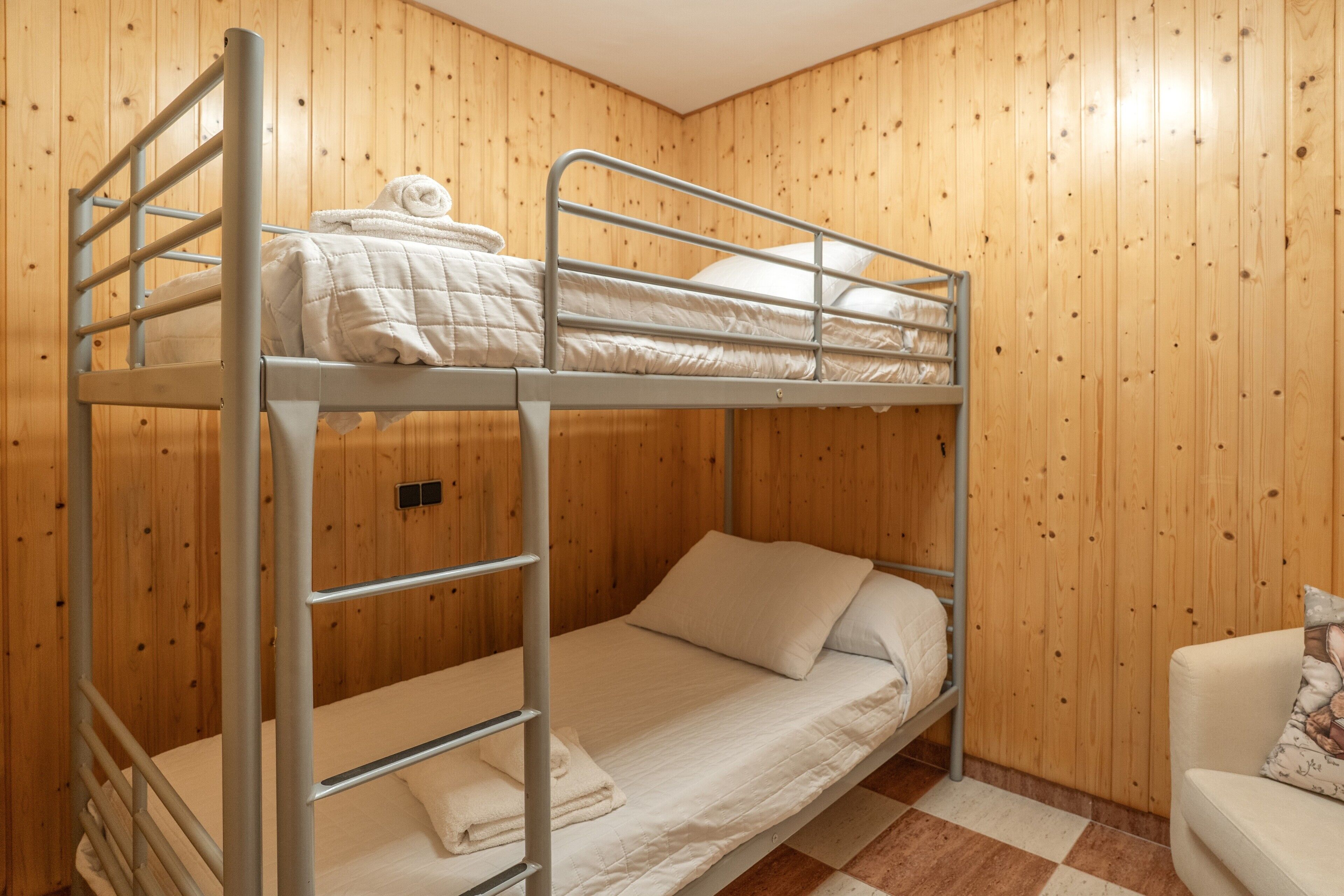 A bunk bed room with wooden walls, a checkered floor, and a white chair.