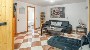 A living room with a checkered floor, a sofa, a coffee table, a bookshelf, and a painting on the wall.