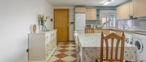 Una cocina con piso a cuadros, armarios de madera, un refrigerador, una lavadora y una mesa de comedor con sillas.