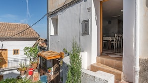 A residential building with a tiled roof, a small balcony with potted plants, and a door leading to an interior with a dining area.