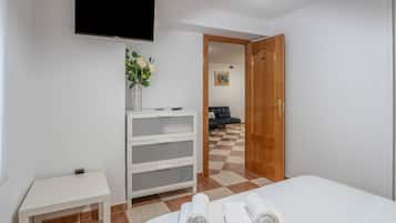 Une chambre d’hôtel avec un lit, un téléviseur fixé au mur, une petite table ornée d’un vase de fleurs et un sol à carreaux.