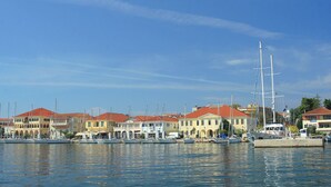 A marina with multiple boats docked, a large sailboat, and buildings with red roofs. - Sun-kissed Sailing Adventure in the Ionian Islands (Preveza)
