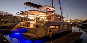 A yacht docked at a marina with a well-lit deck area, a covered seating area, and a floating platform with steps leading to the upper deck. - Sun-Kissed Sailing Adventure in Split-Dalmatia, Croatia (Marina)