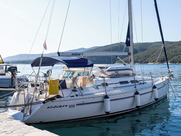 A sailboat named 'elan 333' docked at a marina with clear water and a hilly landscape in the background.