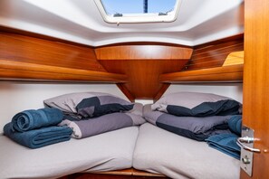 Interior compacto de barco com cama, almofadas e claraboia.