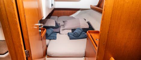 A compact boat interior with a bed, storage compartments, and a small seating area.