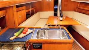 Una cocina pequeña con un lavamanos, una tabla de cortar con verduras y una botella de vino sobre la mesa.
