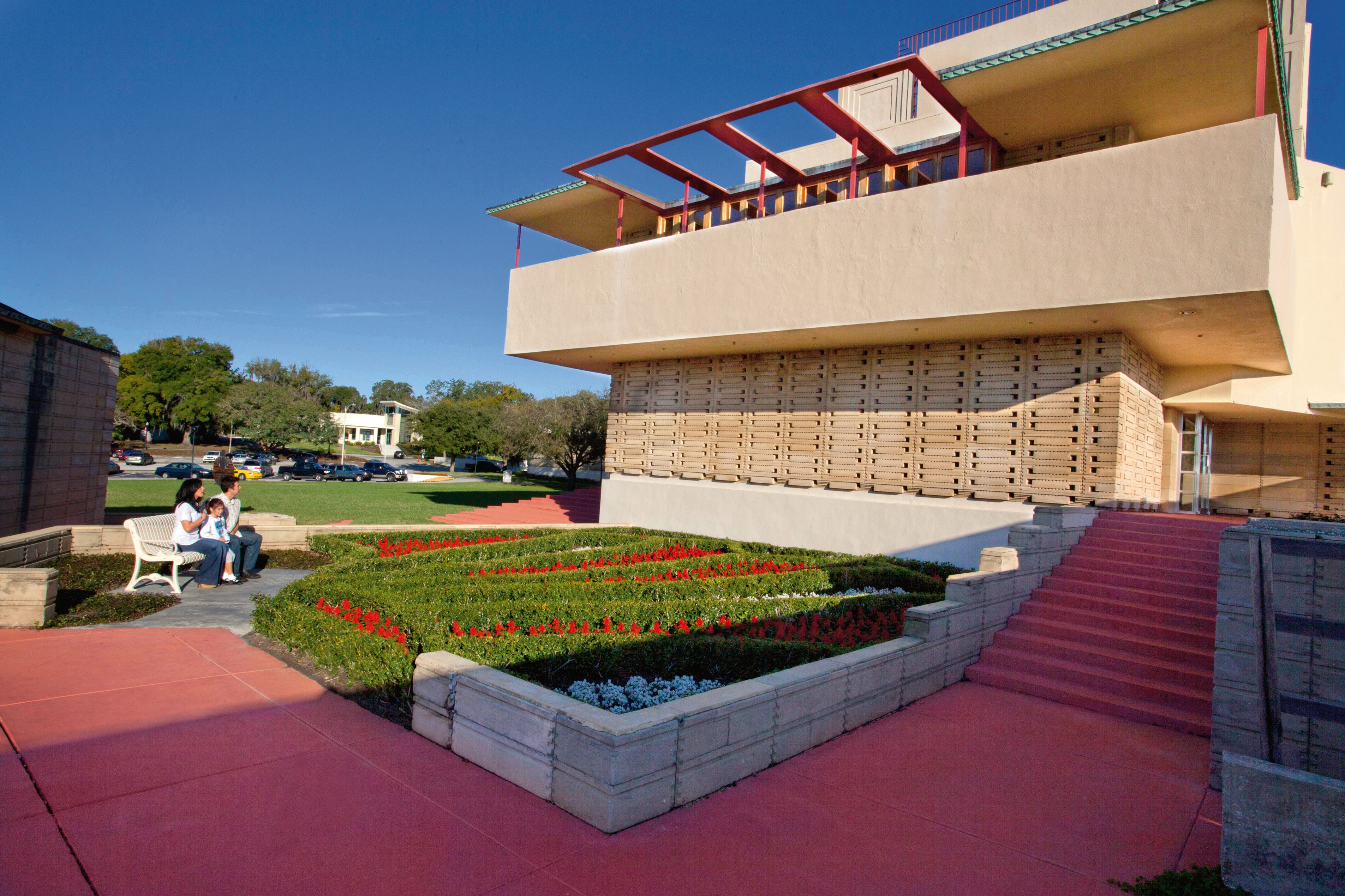 A modern building with a unique architectural design, featuring a prominent overhang and a landscaped garden with red flowers.
