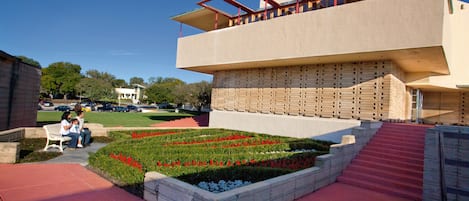 A modern building with a unique architectural design, featuring a prominent overhang and a landscaped garden with red flowers.