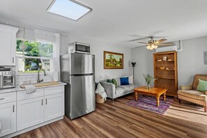 Eine kompakte Küche mit Kühlschrank, Backofen und Mikrowelle. Ein Essbereich mit Tisch und Stühlen, eine Sitzecke und ein Deckenventilator sind ebenfalls vorhanden.