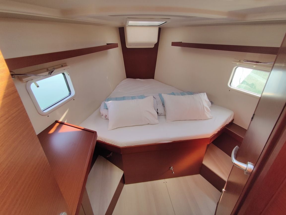 A compact, well-lit interior with a bed, two small windows, and a wooden cabinet.