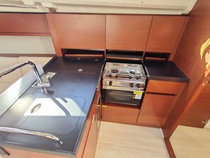A compact kitchenette with a sink, stove, oven, and wooden cabinetry. - Sun-Kissed Sailing Adventure in Zadar, Croatia (Bibinje)