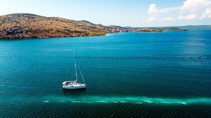 A calm lake with a sailboat, surrounded by hills and a distant shoreline. - Sun-Kissed Sailing Adventure in Sibenik, Croatia (Zaton)