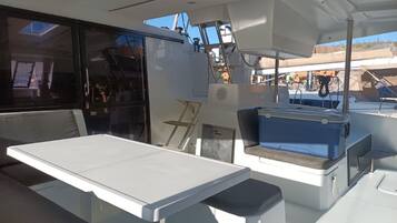 A boat interior with a table, seating, and a cooler.