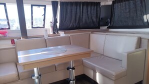 Espaço interior compacto com área de estar acolchoada, uma pequena mesa e uma janela com cortinas.