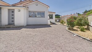 Una propietat residencial amb un carrec de grava, façana blanca i un petit jardí amb flors roses.