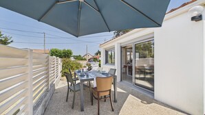 Terrassa exterior amb taula i cadires, un parasol gran i una porta corredissa de vidre que dona a una zona coberta.