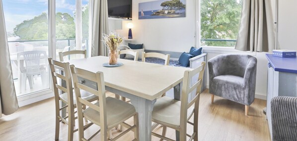 A room with a dining table, chairs, a sofa, a grey armchair, a vase with flowers, and a painting on the wall. - L'Amirauté   4/5 pers I Piscine I Parking inclus (Les Sables-d´Olonne)