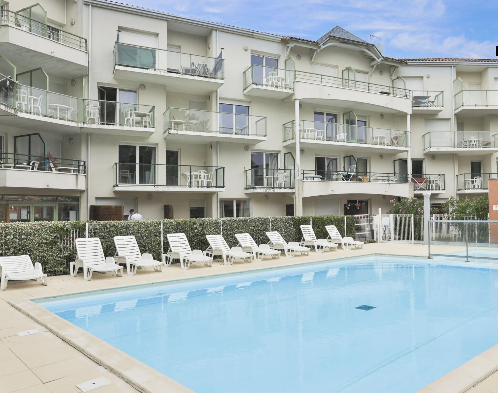 Ein mehrstöckiges Hotel mit Balkonen, einem Schwimmbecken und Liegestühlen.