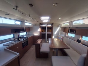 A compact kitchen with a stove, sink, and counter, a dining area with a table and benches, and a small seating area with cushions. - Sun-Kissed Sailing Adventure in the Ionian Islands, Lefkada (Lefkada)