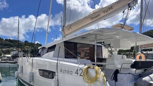A yacht named 'Astreá 42' docked at a marina with other boats, a clear sky, and a mountainous landscape in the background. - Caribbean Bliss: Sun-soaked Sailing Adventure from Granada, San Jorge (Saint George's)