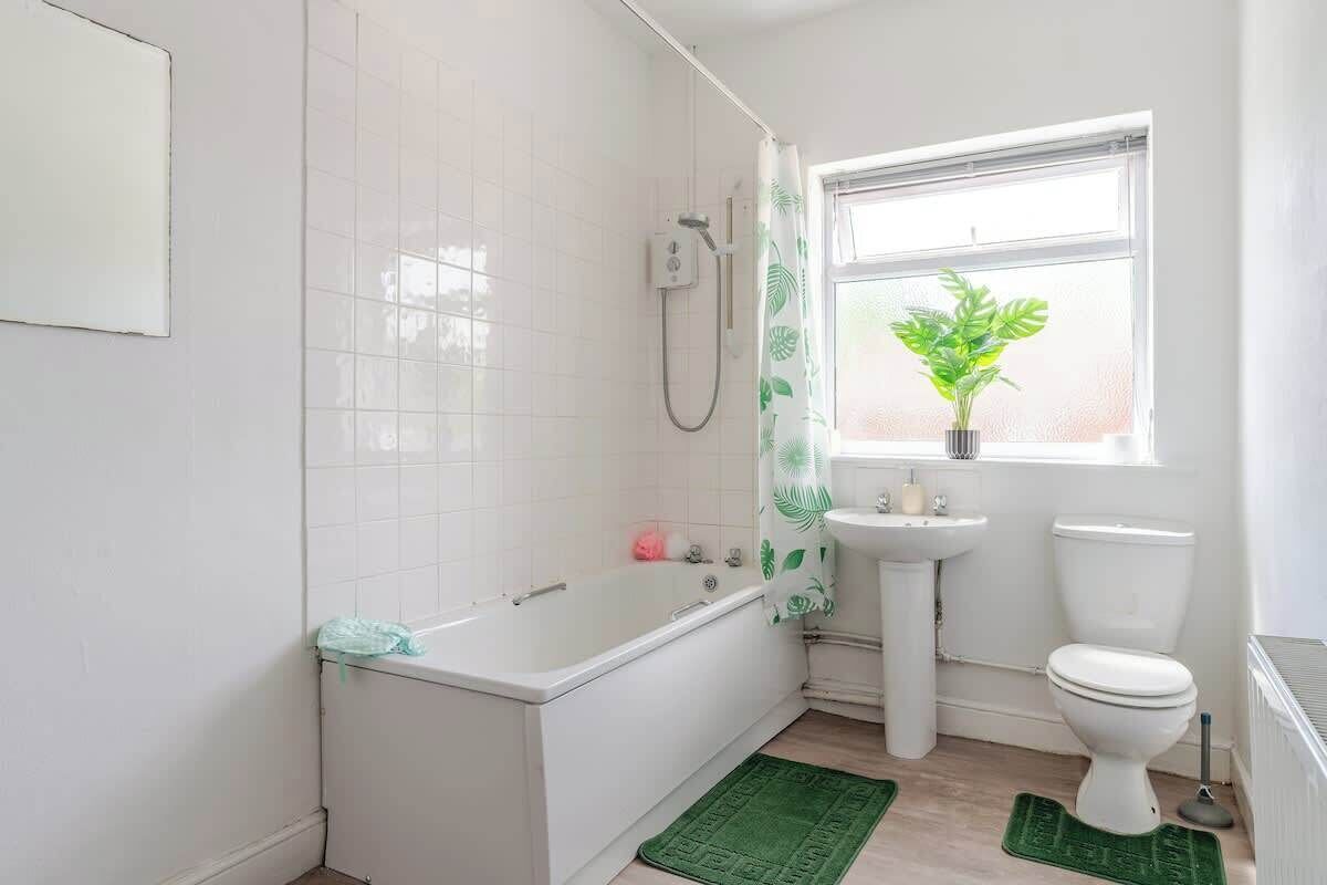 Een badkamer met een bad, wastafel, toilet en een raam met een plant.