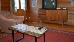 Kodikas olohuone, jossa on televisio, sohva, kaappi ja kuviollinen sohvapöytä.