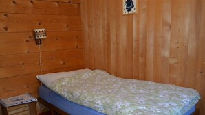 Yhden hengen sänky, jossa on kukallinen päiväpeite, pieni yöpöytä ja seinään kiinnitetty valaisin.