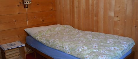 A single bed with a floral bedspread, a small bedside table, and a wall-mounted light fixture.