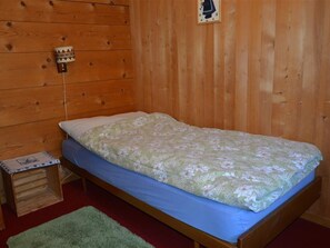 Ein Einzelbett mit blumigem Überwurf, ein kleiner Nachttisch und eine Wandleuchte.