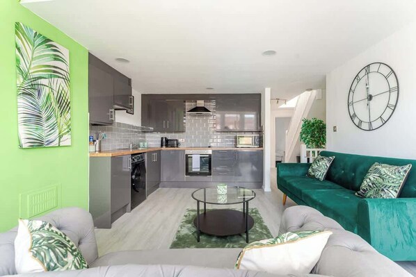 Une cuisine moderne avec des meubles de couleur grise, un îlot central et un canapé vert agrémenté de coussins à motifs.