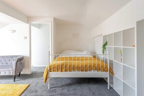 Une chambre à coucher avec un lit, un canapé gris, une armoire blanche et une porte qui donne sur une autre pièce.