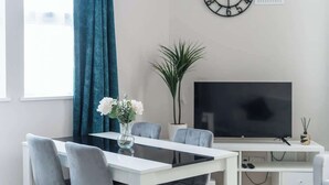 A modern living room with a dining table, chairs, a TV, and a clock on the wall. - Central Bristol Luxury Apartment w/ Fast WiFi, (Redfield)