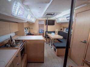 A compact kitchen with a stove, sink, and a small dining area with a table and bench. - Sun-Kissed Sailing Adventure in Zadar, Croatia (Zadar)