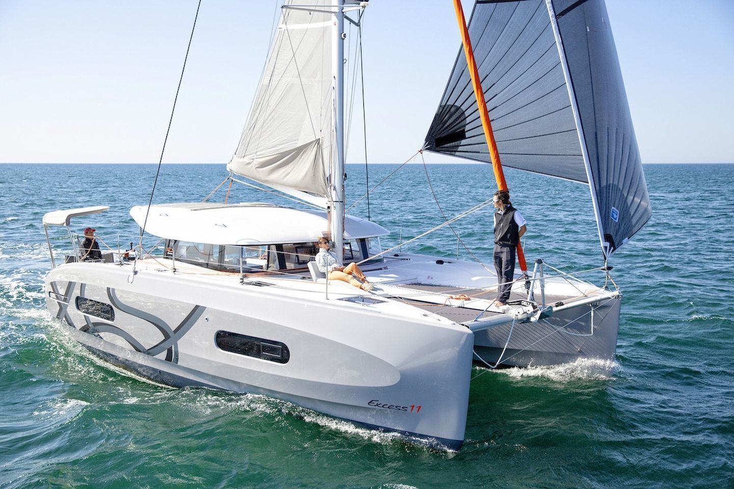 Un velero con casco blanco y camarote, llamado 'Excess 11', sobre el agua.