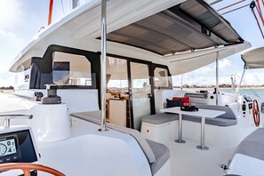 A boat's deck with a steering wheel, a table with cushions, and a small kitchen area. - Caribbean Bliss: Sun-Soaked Sailing Adventure from San Martín, Anse Marcel (Anse Marcel)