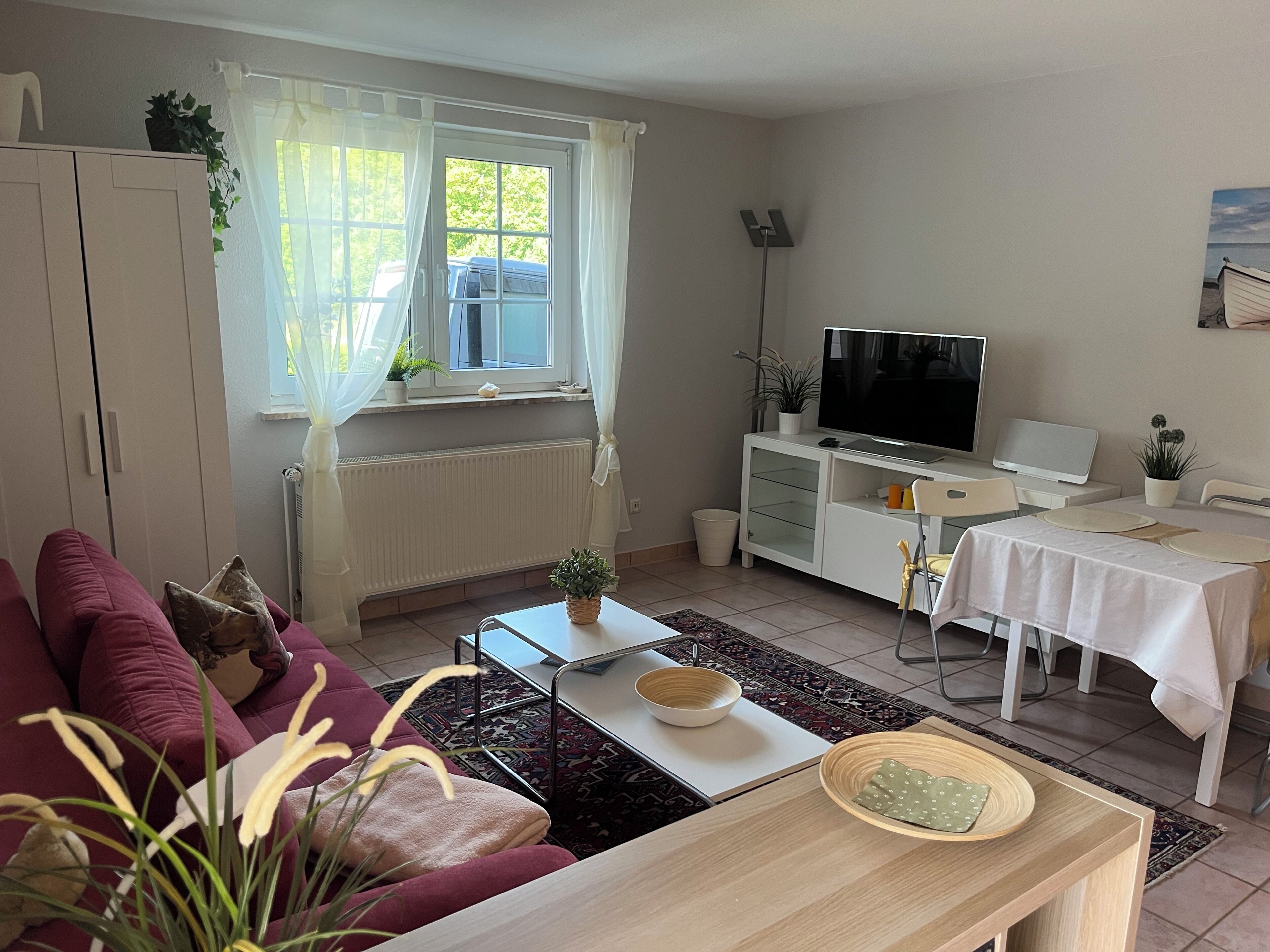 Ein Wohnzimmer mit einer Couch, einem Couchtisch, einem Fernseher, einem Esstisch und einer Heizung.