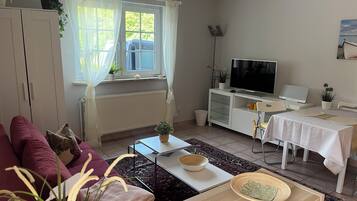 Ein Wohnzimmer mit einer Couch, einem Couchtisch, einem Fernseher, einem Esstisch und einer Heizung.