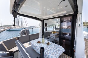 Het dek van een boot met een tafel voor twee, een champagneflesje en uitzicht op de jachthaven.