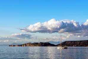 A calm sea with a sailboat, rocky coastline, and distant mountains under a partly cloudy sky. - Sun-Kissed Sailing Adventure in Peloponeso (Kiato)