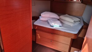 A compact bed with pillows and folded blankets, a wooden nightstand, and a drawer. - Sun-Kissed Sailing Adventure in Sibenik, Croatia (Zaton)