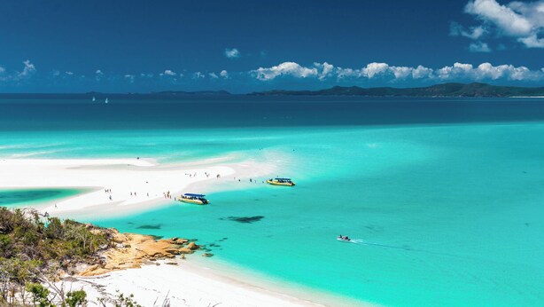 Un paisaje costero con aguas turquesas cristalinas, una playa arenosa y barcos.