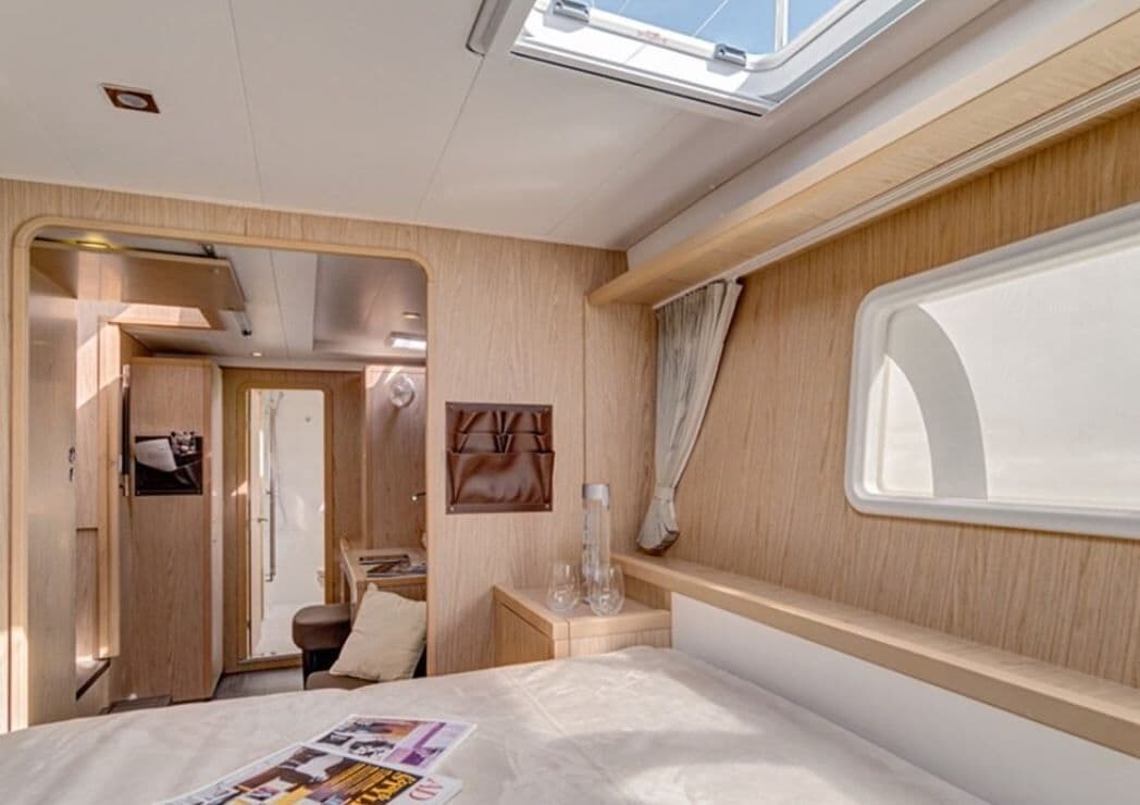 A compact RV interior with a bed, a small table, a window, and a door leading to an external area.
