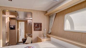 A compact RV interior with a bed, a small table, a window, and a door leading to an external area.