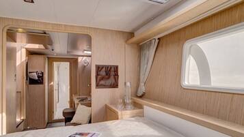 A compact RV interior with a bed, a small table, a window, and a door leading to an external area.