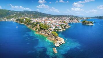 An aerial view of a coastal town with buildings, clear blue waters, and a hilly landscape in the background.